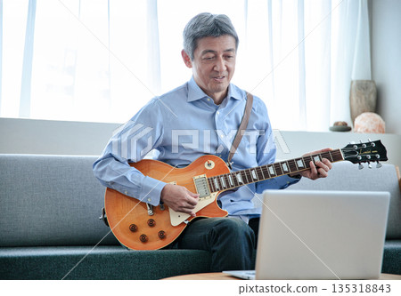 一位老年男子正在用筆記型電腦上線上吉他課 135318843