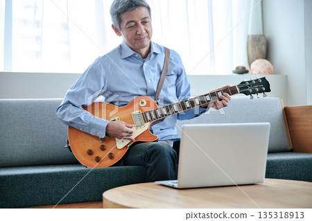 一位老年男子正在用筆記型電腦上線上吉他課 135318913