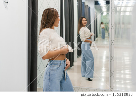 Woman Checking Fit Of Jeans In Dressing Room Woman Checking Fit Of Jeans In Dressing Room 135318953