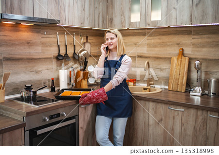 Cooking in a modern kitchen while chatting on the phone with a friend 135318998