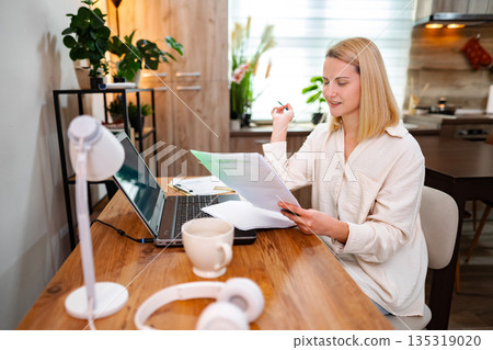 Focused woman working at home office while reviewing important documents Focused woman working at home office while reviewing important documents 135319020