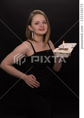 A woman in a black dress blows out a candle on a bento cake. Smoke on a black background. A girl's birthday, happiness, a gift. High quality photo A woman in a black dress blows out a candle on a bento cake. Smoke on a black background. A girl's birthday, happiness, a gift. High quality photo 135319273