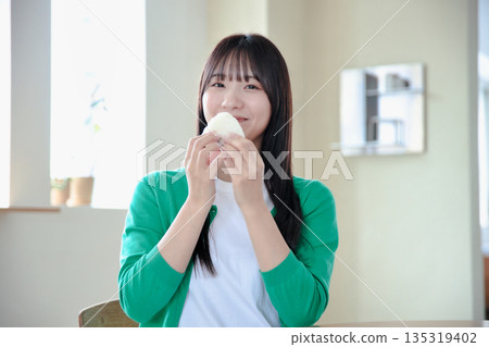 一位年輕女子津津有味地吃著飯糰。 一位年輕女子津津有味地吃著飯糰。 135319402