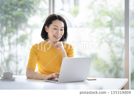 A woman in her early 50s working on a laptop 135319809