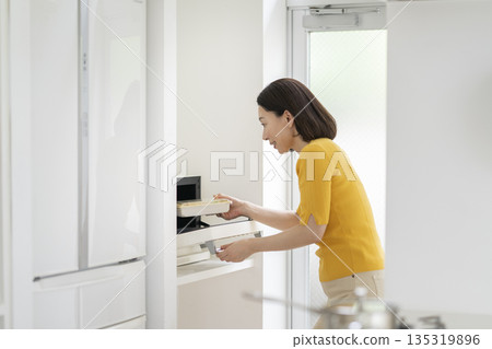 A woman in her 50s warming up her lunch in the microwave 135319896