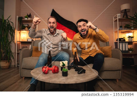 Friends celebrating a sports victory with enthusiasm at home in a cozy living room setting during a thrilling match night 135319994
