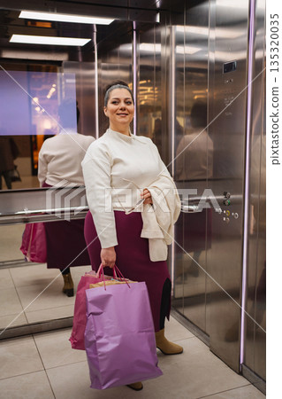Joyful shopper with vibrant bags in a modern elevator setting 135320035
