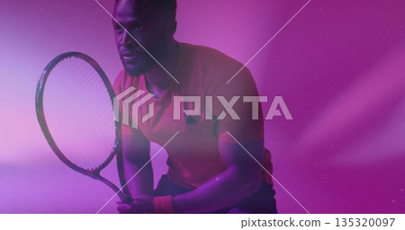 Assuming ready stance tennis player in red shirt in gradient lights, gripping racket with wristband Assuming ready stance tennis player in red shirt in gradient lights, gripping racket with wristband 135320097
