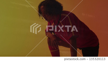 Crouching female athlete holding ready stance in studio, with red jersey, black shorts, red socks 135320113