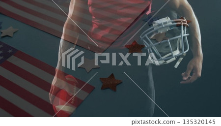 Holding football and helmet, male athlete wearing jersey posing at studio, with flag and stars Holding football and helmet, male athlete wearing jersey posing at studio, with flag and stars 135320145