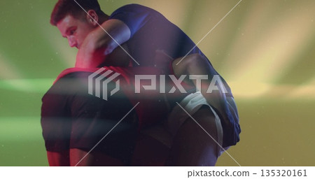 Lifting male athlete carrying partner in performance studio, with colored lights and sportswear 135320161