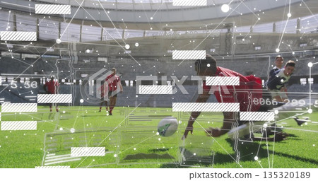 Diving soccer player in red jersey reaching ball on green grass at stadium, with sliding opponents 135320189