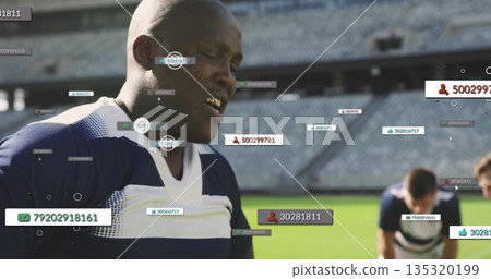 Gasping African American athlete recovering on grass at stadium, with floating digital overlays 135320199