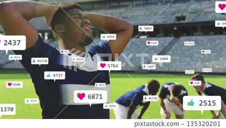 Gripping head soccer player in navy jersey on pitch at stadium, with floating social media icons Gripping head soccer player in navy jersey on pitch at stadium, with floating social media icons 135320201