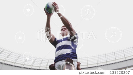 Lifting athlete in blue jersey by teammates catching rugby ball in stadium with floating icons 135320207