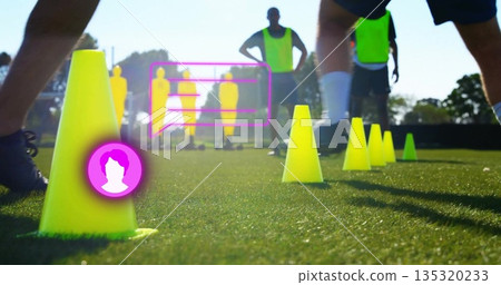 Standing yellow training cones marking pitch, with soccer players practicing near magenta overlays 135320233