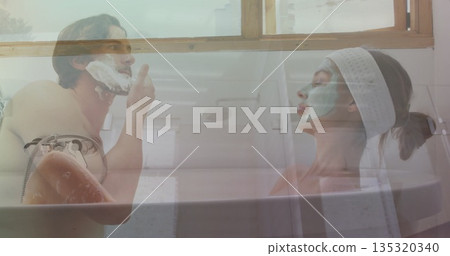 Shirtless man and woman wearing spa headband and facial mask grooming in bathtub, with shaving foam Shirtless man and woman wearing spa headband and facial mask grooming in bathtub, with shaving foam 135320340