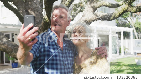 Taking selfie, sweater-clad woman and plaid-shirt man under oak tree in backyard, with smartphone Taking selfie, sweater-clad woman and plaid-shirt man under oak tree in backyard, with smartphone 135320363