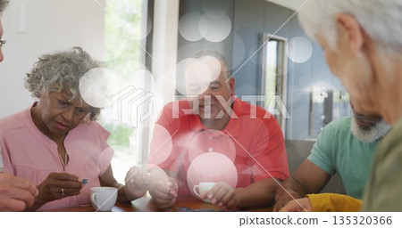 Putting together jigsaw puzzle pieces by four friends in living area, with table mugs eyeglasses 135320366
