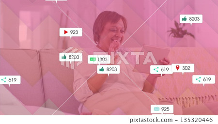 Waving mature woman using tablet, sitting on sofa in living room, displaying social metrics Waving mature woman using tablet, sitting on sofa in living room, displaying social metrics 135320446