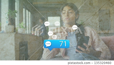 Reclining teenage girl using smartphone with chat icons on couch by marble countertop, potted plant 135320460