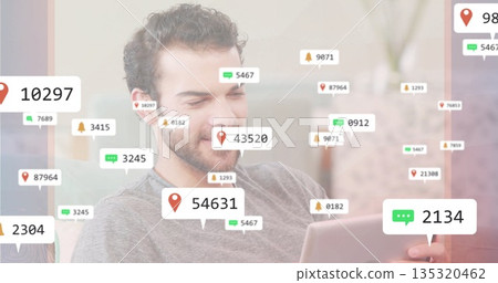 Checking tablet, man wearing grey top interacting with floating notification icons in living room 135320462
