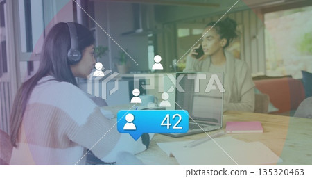 Studying teenager wearing headphones using laptop at kitchen table with social icons, copy space 135320463