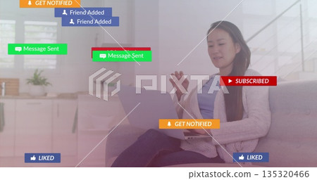 Interacting Korean woman using silver laptop on light grey couch at home, with floating overlays Interacting Korean woman using silver laptop on light grey couch at home, with floating overlays 135320466