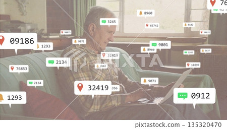 Typing senior man on laptop on sofa in living room, with floating notification icons Typing senior man on laptop on sofa in living room, with floating notification icons 135320470