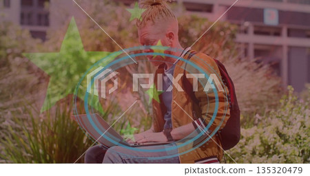 Working student typing on laptop at urban courtyard steps, wearing bomber jacket with backpack Working student typing on laptop at urban courtyard steps, wearing bomber jacket with backpack 135320479
