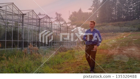 Walking researcher in shirt using tablet in field near greenhouse, world map overlay, copy space Walking researcher in shirt using tablet in field near greenhouse, world map overlay, copy space 135320488