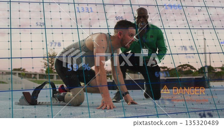 Crouching amputee runner using blade at blocks on track, with coach using device overlaying danger Crouching amputee runner using blade at blocks on track, with coach using device overlaying danger 135320489