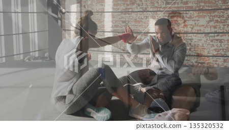 Practicing trainee throwing jab at kneeling trainer in boxing ring with red wraps ropes duffel bag Practicing trainee throwing jab at kneeling trainer in boxing ring with red wraps ropes duffel bag 135320532