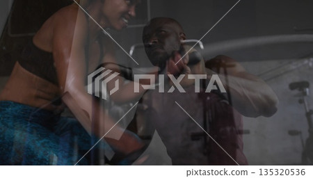 Female trainer leaning close to guide male client doing cable pushdown in gym, with rope attachment 135320536