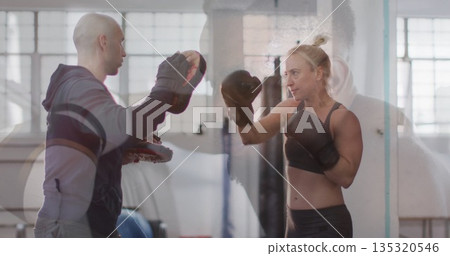 Female trainee wearing boxing gloves punching focus mitts in boxing gym workout area, copy space Female trainee wearing boxing gloves punching focus mitts in boxing gym workout area, copy space 135320546