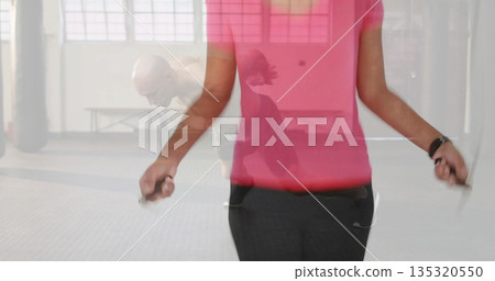 Skipping African American woman wearing pink top using jump rope in gym, with punching bags Skipping African American woman wearing pink top using jump rope in gym, with punching bags 135320550