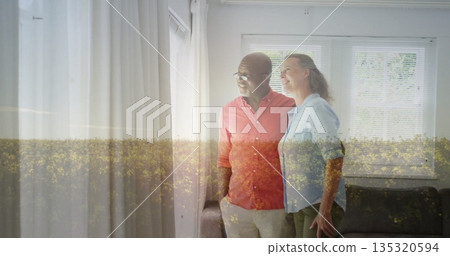 Standing seniors looking through window in living room, curtains, blinds, sofa and yellow overlay 135320594
