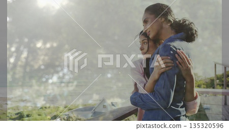 Embracing mother and daughter gazing over sunlit valley on balcony with metal railing, copy space Embracing mother and daughter gazing over sunlit valley on balcony with metal railing, copy space 135320596
