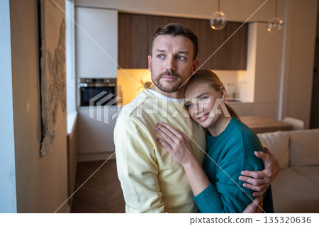 Positive pensive couple man and woman embracing and looking at window with pensive expression. Positive pensive couple man and woman embracing and looking at window with pensive expression. 135320636