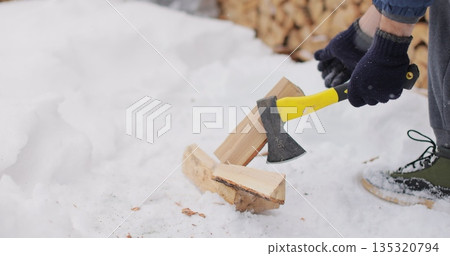 Man is chopping firewood in the backyard of his house. Preparations for cold winter months. 135320794
