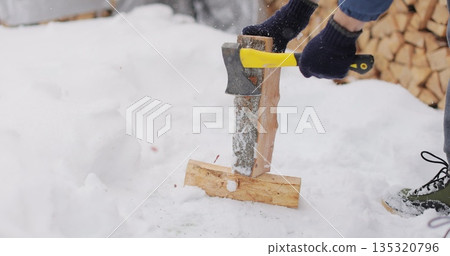 Man is chopping firewood in the backyard of his house. Preparations for cold winter months. 135320796