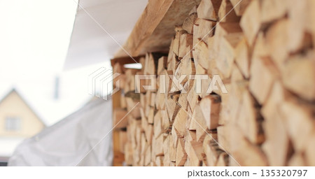Neatly stacked pile of cut firewood arranged under protective roof. Firewood pile. 135320797