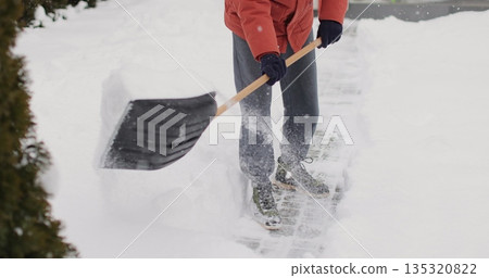 Close up man with a shovel removes snow. cleaning the area near the house after a snowstorm. Close up man with a shovel removes snow. cleaning the area near the house after a snowstorm. 135320822