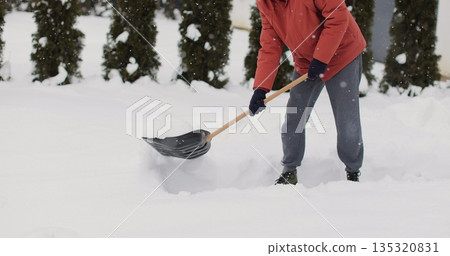 Young man cleans snow with a shovel after snowfall background of the house in winter. 135320831