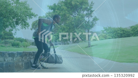 Lifting duffel bag, African American man wearing hoodie and leggings beside park bench, copy space Lifting duffel bag, African American man wearing hoodie and leggings beside park bench, copy space 135320992