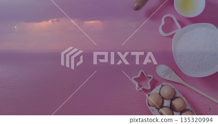 Displaying sea under purple-pink sky and baking setup on pink surface with flour bowl, copy space 135320994