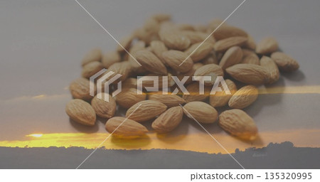 Displaying heap of tan whole almonds reflecting on smooth tabletop, with sunset hill silhouette Displaying heap of tan whole almonds reflecting on smooth tabletop, with sunset hill silhouette 135320995