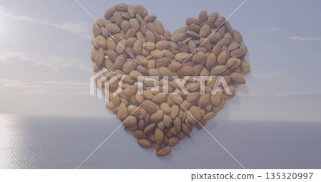 Heart-shaped cluster of whole almonds resting on shore at coastal vista, with calm ocean reflection Heart-shaped cluster of whole almonds resting on shore at coastal vista, with calm ocean reflection 135320997