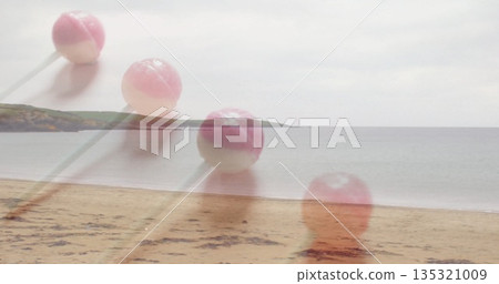Four translucent round pink-and-white lollipops with sticks drifting above sandy beach, cloudy sky 135321009
