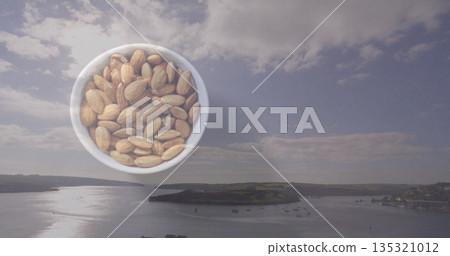 Floating white ceramic bowl holding unshelled almonds over coastal harbor waters, with moored boats Floating white ceramic bowl holding unshelled almonds over coastal harbor waters, with moored boats 135321012